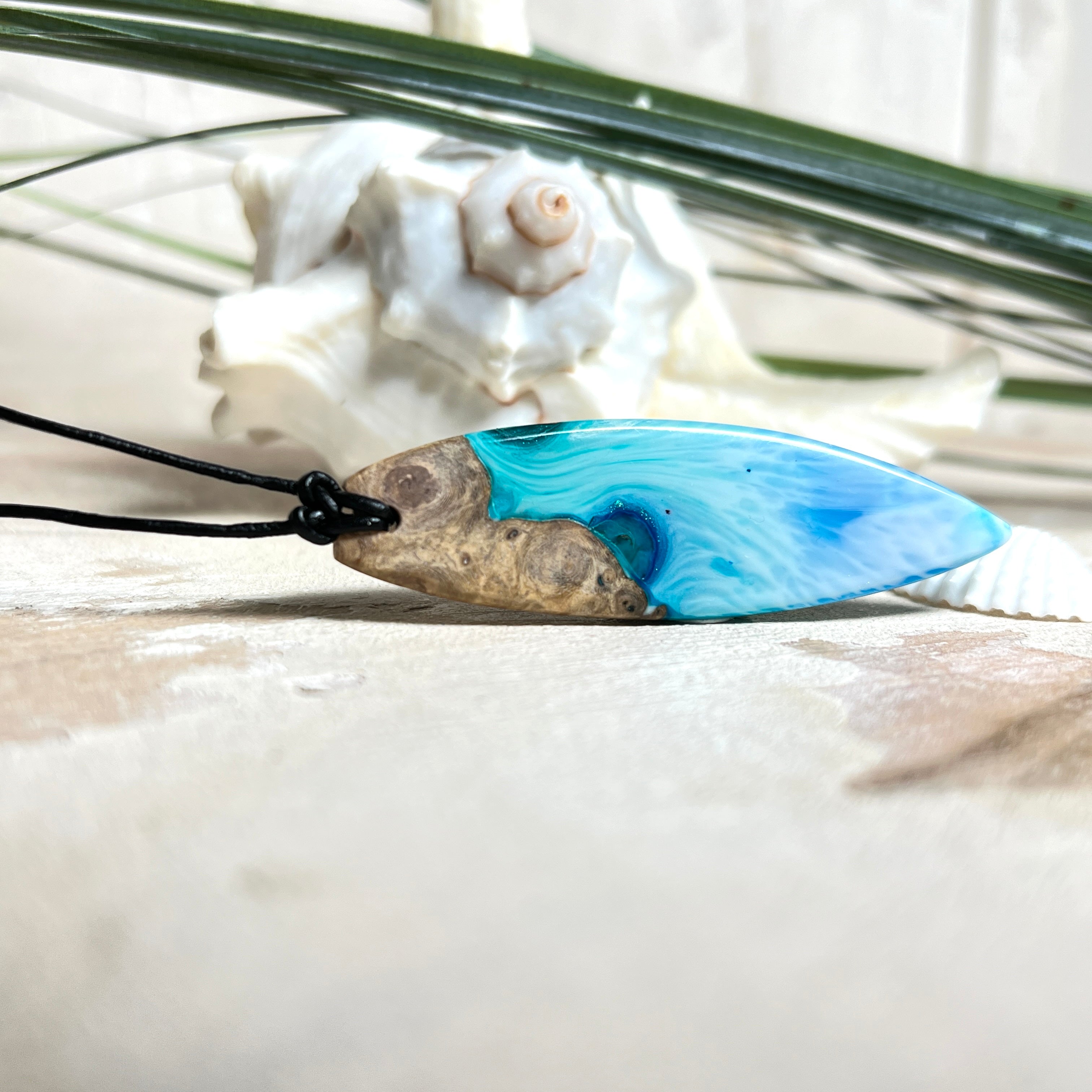 Surfbrett-Anhänger handgefertigt aus Maserholz & Harz in Blau-Weiß. Größe ca. 6,3 × 2 cm. Lederband verstellbar 26–47 cm, Schiebeknoten mit Holzperlen.