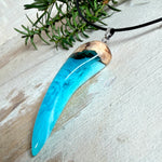 Handgefertigter Anhänger aus Edelholz und transparent-türkisblauem und weißen Epoxidharz, glatt poliert. Größe ca. 6,5 × 2,0 cm. Mit Edelstahlöse an schwarzer Lederkette (45 cm + 5 cm Edelstahl-Verlängerung, Karabiner). Moderner, unisex tragbarer Schmuck mit natürlicher Holzmaserung; kleine Lufteinschlüsse sind charakteristisch.