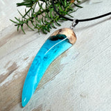 Handgefertigter Anhänger aus Edelholz und transparent-türkisblauem und weißen Epoxidharz, glatt poliert. Größe ca. 6,5 × 2,0 cm. Mit Edelstahlöse an schwarzer Lederkette (45 cm + 5 cm Edelstahl-Verlängerung, Karabiner). Moderner, unisex tragbarer Schmuck mit natürlicher Holzmaserung; kleine Lufteinschlüsse sind charakteristisch.