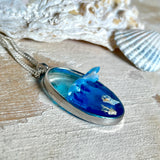 „Riffschatz“ – ovaler Harz-Anhänger mit plastischer 3D-Welle in Blau/Türkis, weißer Schaumkrone und Muschel-/Korallen-Stickern am Grund. Die Sticker sind unter klarem Harz versiegelt. Silber-Legierung, ca. 3,9 × 2,3 cm, an einer ca. 56 cm langen versilberten Kette. Handgefertigt, hochglänzend, jedes Stück ein Unikat.