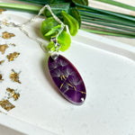 Ovaler Anhänger mit echter Pusteblume in Harz, Hintergrund Brombeerfarben. Größe 4 × 1,8 cm, versilberte Kette 50 cm mit Karabinerverschluss. Handgefertigtes Unikat.
