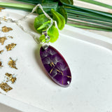 Ovaler Anhänger mit echter Pusteblume in Harz, Hintergrund Brombeerfarben. Größe 4 × 1,8 cm, versilberte Kette 50 cm mit Karabinerverschluss. Handgefertigtes Unikat.
