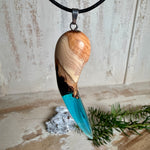 Handgefertigter Anhänger aus Edelholz und transparent-türkisblauem Epoxidharz, glatt poliert. Größe ca. 6,7 × 2,0 cm. Mit Edelstahlöse an schwarzer Lederkette (45 cm + 5 cm Edelstahl-Verlängerung, Karabiner). Maritimer, moderner Unisex-Schmuck mit natürlicher Holzmaserung; kleine Lufteinschlüsse sind charakteristisch.