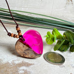 Handgefertigter Herzanhänger aus Olivenholz und leuchtend pinkem Epoxidharz mit eingeschlossenen Pusteblumensamen. Verstellbares braunes Lederband mit Holzperlen, Anhänger ca. 3,5 × 3,3 cm groß. Das Harz leuchtet dezent unter Schwarzlicht. Ein einzigartiges Unikat von ZeitlosSchmuckDesign, inspiriert von Kindheitsglück und Pusteblumen.