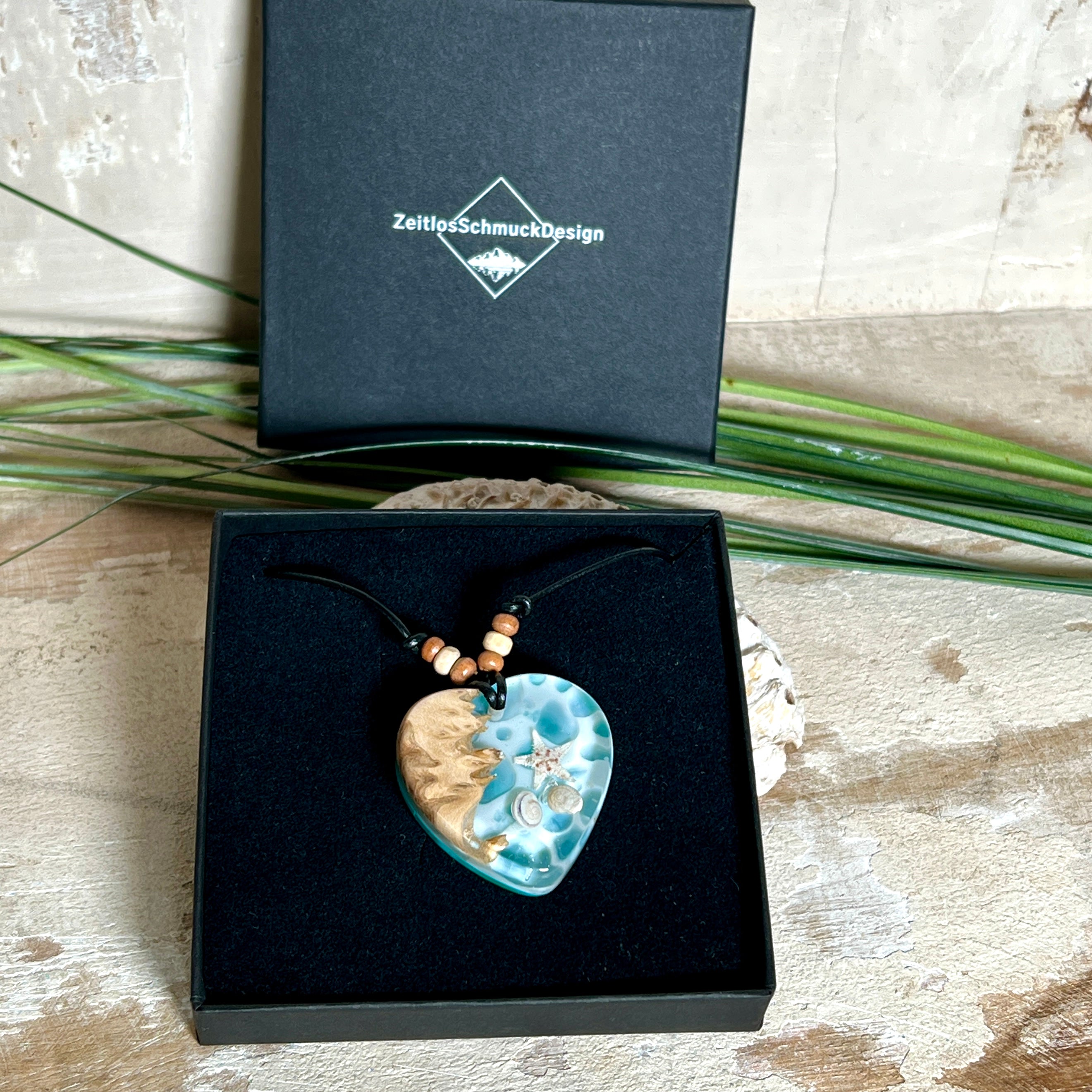 Handgefertigter Herzanhänger aus Maserholz und transparentem Ocean-Harz mit echtem Seestern und Muscheln. Die zarten Aqua-Farben erinnern an Meereswellen. Lederband verstellbar mit Holzperlen. Größe ca. 3,5 × 3,2 cm. Natürliches, maritimes Unikat von ZeitlosSchmuckDesign
