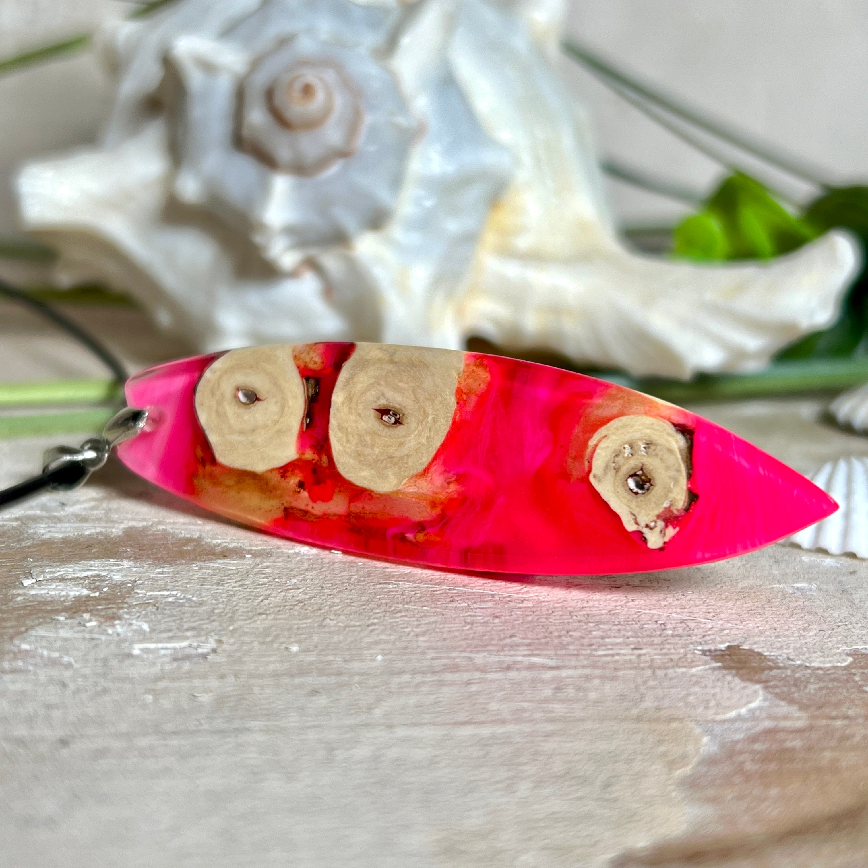 Handgefertigter Surfbrett-Anhänger „Flame Surf“ aus Maserholz und fluoreszierendem Harz in kräftigem Pink. Das Schmuckstück leuchtet bei Schwarzlicht und wird an einer schwarzen Lederkette mit Edelstahl-Karabiner (45 cm + 5 cm Verlängerung) geliefert. Größe ca. 6,7 × 2 cm. Ein Unikat für Surf- und Strandliebhaber, edel verarbeitet und mit Liebe gefertigt.