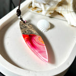 Aurora Flame – fluoreszierender Surfbrett-Anhänger aus Maserholz und leuchtendem Epoxidharz in Rosa, Pink, Orange und Weiß. Der handgefertigte Unikat-Anhänger fluoresziert bei Schwarzlicht in intensiven Farbtönen. Er ist ca. 6,3 x 2 cm groß, wird an einem verstellbaren Lederband (26–45 cm) getragen und ist mit einer silberfarbenen Spacerperle verziert. Ein ausdrucksstarkes Schmuckstück für Menschen mit Persönlichkeit.