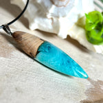 Anhänger aus Eibenholz und Epoxidharz in Blau-Türkis, Weiß und Transparent. Größe ca. 5,8 × 2 cm, Edelstahlöse, Lederkette 45+5 cm. Handgefertigtes Unikat inspiriert vom Ozean.