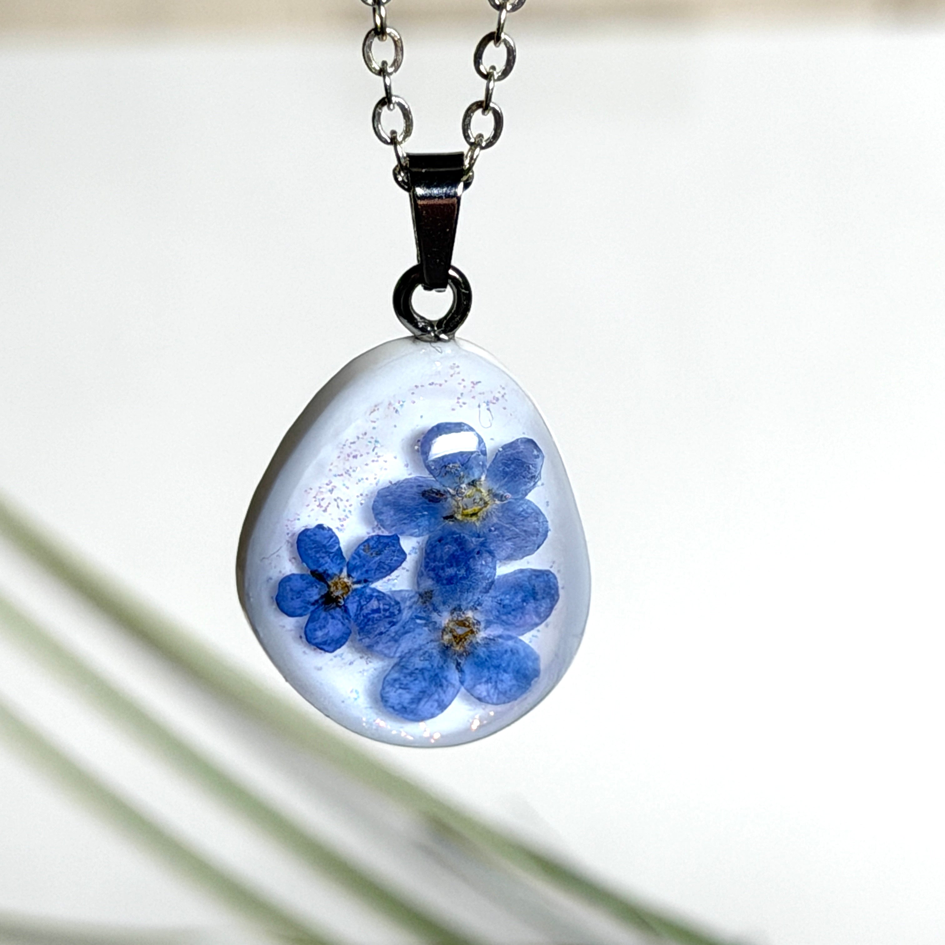Anhänger aus weißem Epoxidharz mit echten gepressten Vergissmeinnichtblüten und einem Hauch feinem Glitzer – romantisch, handgefertigt und unvergänglich schön. Versilberte Kette ca. 46 cm, Edelstahl-Karabiner.