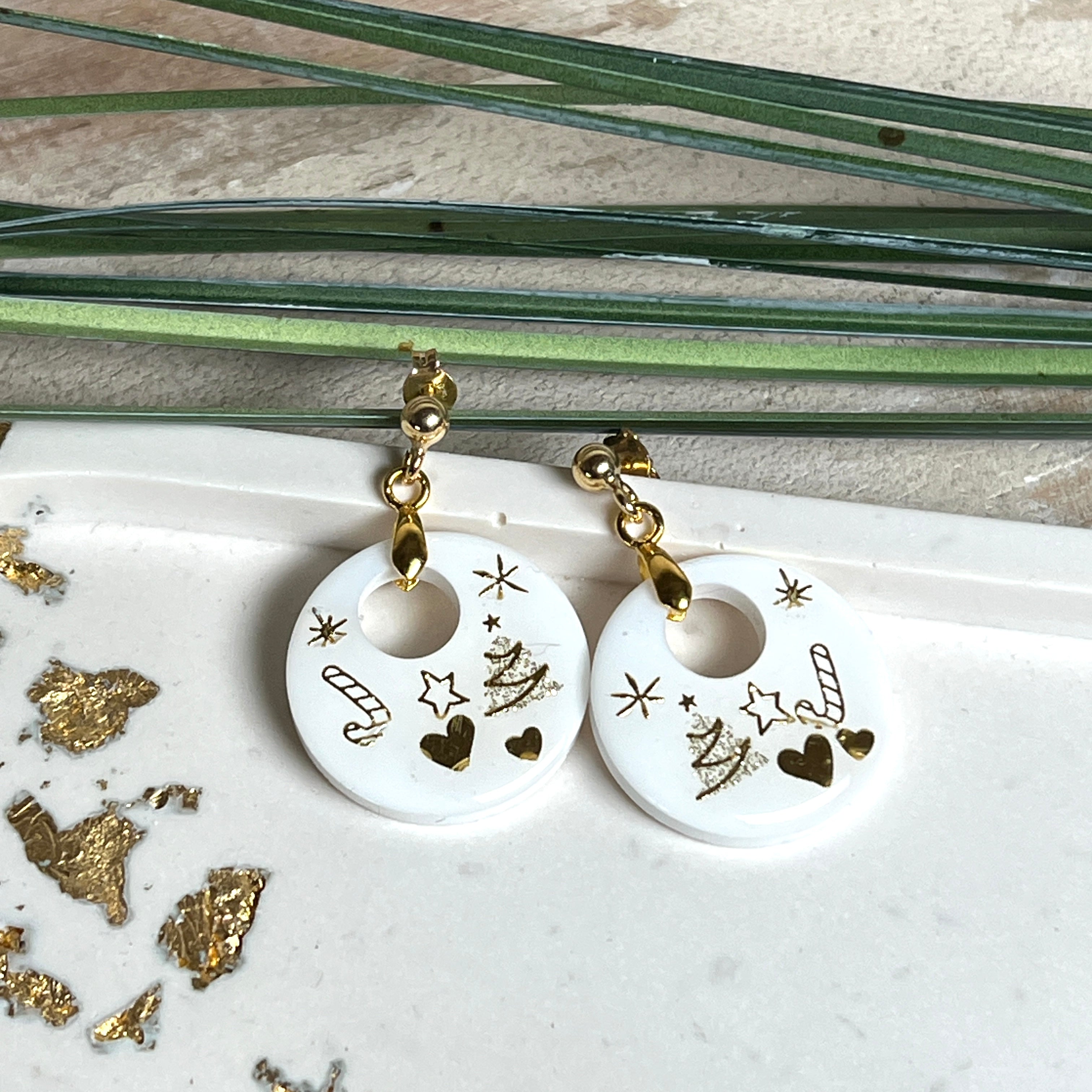 Handgefertigte Ohrringe aus weißem und klarem Harz mit goldenen Weihnachtsmotiven – Sterne, Herzen, Tannenbaum und Zuckerstange. Ohrstecker aus 925 Silber vergoldet, Anhängerschlaufe vergoldet. Größe ca. 37 mm × 25 mm. Leichte, elegante Festtagsohrringe mit warmem Goldglanz und winterlicher Ausstrahlung.