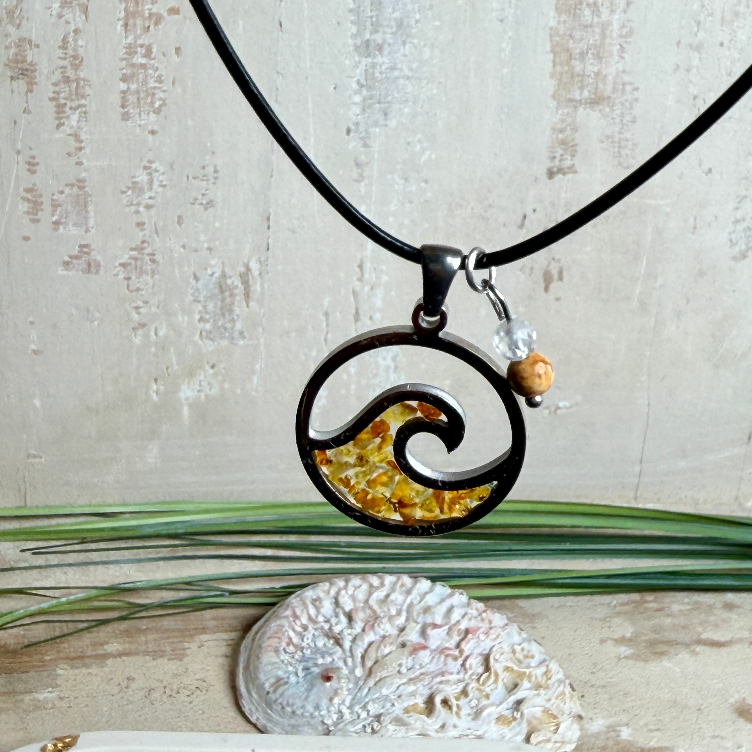 “Runder Wellenanhänger aus Edelstahl mit Bernstein-Harz-Inlay, Jaspisperle & facettiertem Bergkristall an schwarzer Lederkette (45 cm + 5 cm).”