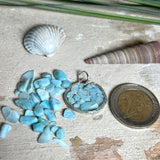 Runder Anhänger „Atlantis Dream“ aus antik-silberfarbener Zinklegierung, gefüllt mit kleinen Larimar-Edelsteinchen und klarem Resin. Die Larimarsteine zeigen sanfte Blau- und Weißtöne, die an das Meer erinnern. Durchmesser ca. 22 mm, handgefertigtes Unikat, fotografiert auf maritimem Untergrund mit kleinen Larimarsteinen und Muscheln zur Größenorientierung.