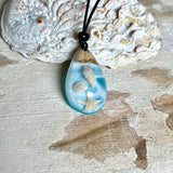 Handgefertigter Tropfenanhänger aus Maserholz und klarem Epoxidharz in Aquatönen. Im Harz sind echte Muscheln und ein kleiner Seestern eingebettet. Durch die besondere Mehrschicht-Gießtechnik wirkt es, als würden die Muscheln im Wasser schweben. Größe ca. 3,8 × 2 cm. Verstellbares Lederband (24–44 cm) mit Holzperlen. Maritimes Unikat.