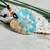 Handgefertigter Herzanhänger aus Maserholz und transparentem Ocean-Harz mit echtem Seestern und Muscheln. Die zarten Aqua-Farben erinnern an Meereswellen. Lederband verstellbar mit Holzperlen. Größe ca. 3,5 × 3,2 cm. Natürliches, maritimes Unikat von ZeitlosSchmuckDesign