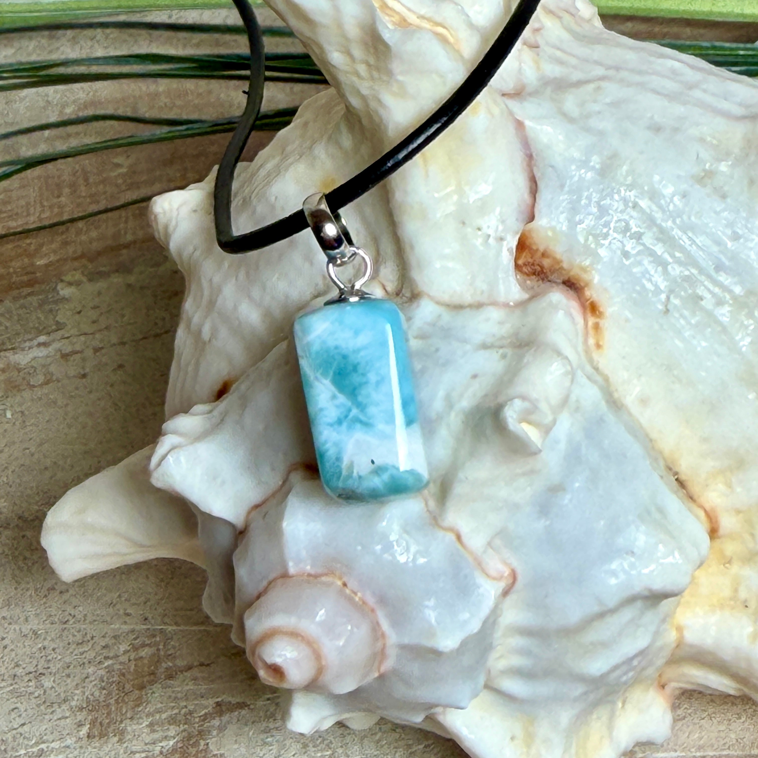 Larimar Freeform Anhänger an schwarzer Lederkette. Natürlicher, rechteckiger Larimar-Stein (ca. 1,5 × 1 cm) in Türkis-Blau mit weißen Strukturen, eingefasst in eine rhodinierte Silberöse. Beidseitig tragbar, an 45 cm Lederkette mit Edelstahl-Karabinerverschluss und 5 cm Verlängerung. Maritimes, zurückhaltend elegantes Schmuckstück mit der Optik karibischen Meerwassers.