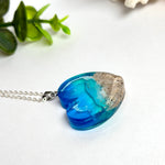 Ein herzförmiger Anhänger mit einer ganzen Ozeanwelt darin: Welle, Sand und Seestern in leuchtendem Blau und Türkis – handgegossen, einzigartig, unvergesslich. Mit versilberter Kette (46 cm) und Edelstahl-Karabiner.