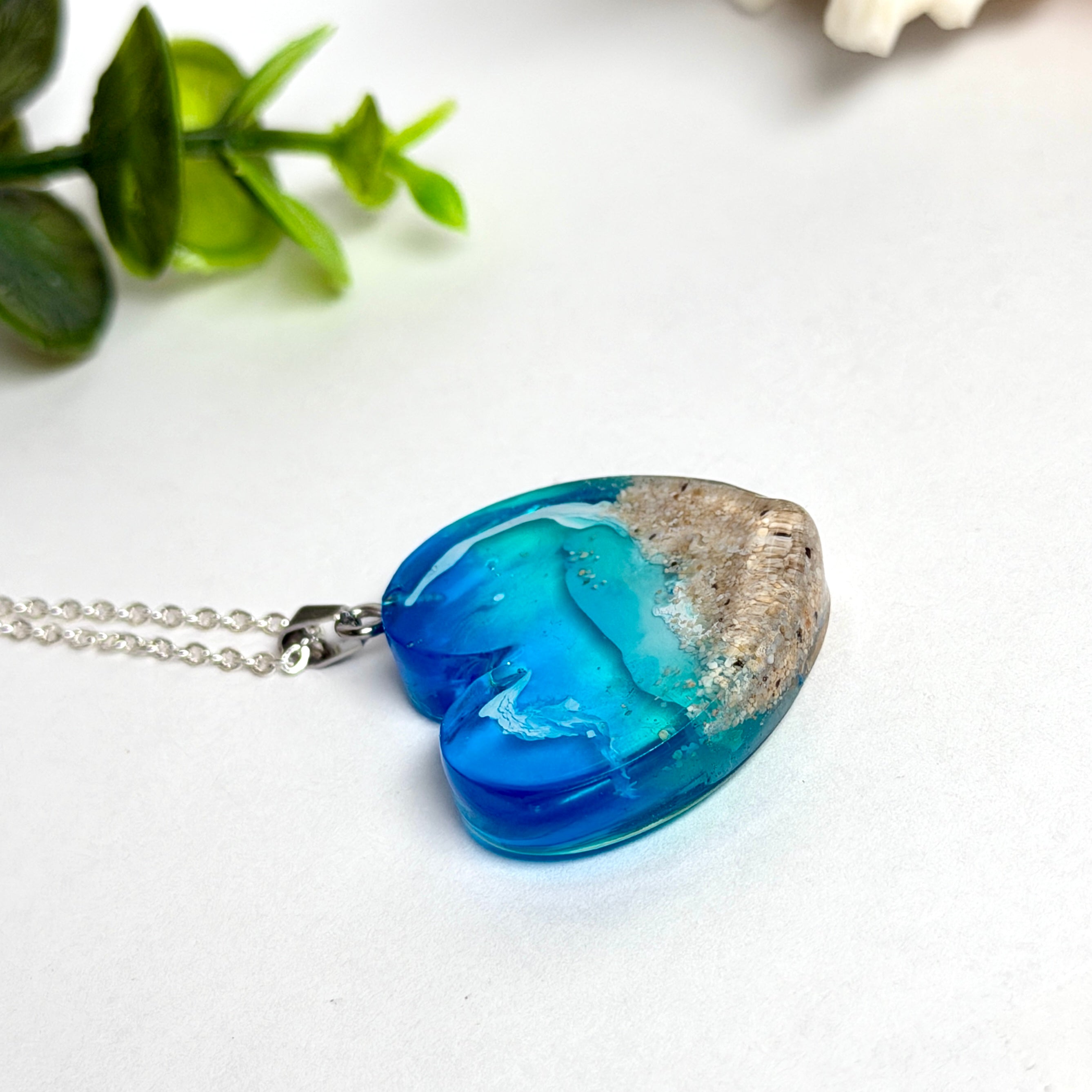 Ein herzförmiger Anhänger mit einer ganzen Ozeanwelt darin: Welle, Sand und Seestern in leuchtendem Blau und Türkis – handgegossen, einzigartig, unvergesslich. Mit versilberter Kette (46 cm) und Edelstahl-Karabiner.