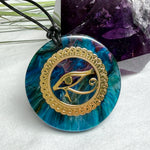 Runder Anhänger mit goldenem Horusauge aus Metall in blau türkis violettem Epoxidharz am schwarzen Baumwollband, spiritueller Eye of Ra Naturschmuck Amulett
