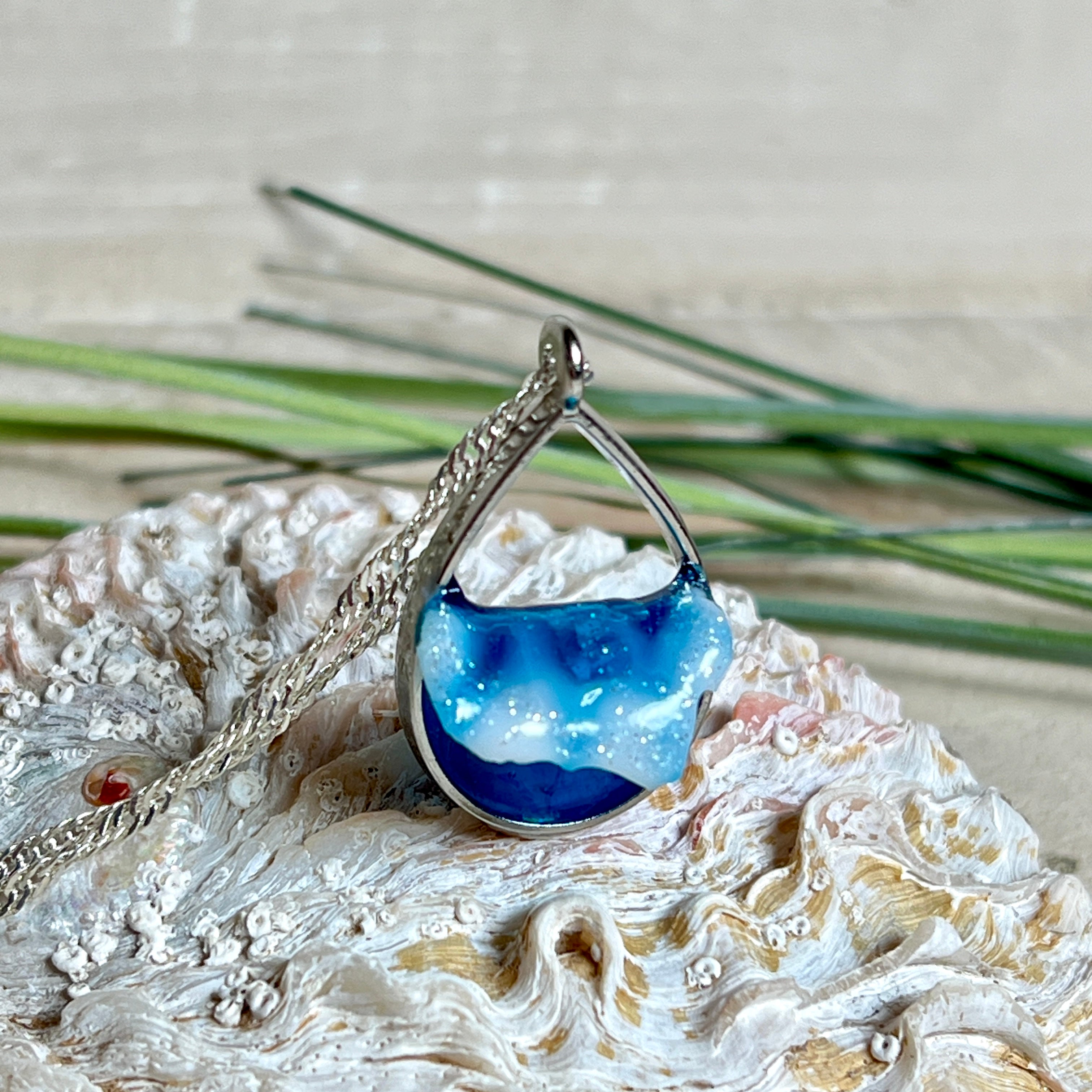 „Lagunenlicht“ – Tropfenanhänger mit handmodellierter 3D-Welle und feinem Glitzereffekt. Klarer Harzlook in Blau/Türkis, gefasst in Silber-Legierung. Größe ca. 3,5 × 2 cm. Geliefert an einer versilberten Kette (ca. 56 cm). Hochglänzend , maritimer Unikatcharakter.