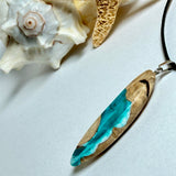 Handgefertigte Surfbrett Kette aus Maserholz und türkisfarbenem Resin mit Edelstahl Anhängerschlaufe an schwarzer Lederkette mit Karabiner und Verlängerung. Filigraner Ocean Anhänger inspiriert von Meer und Wellen, natürlicher Unikat Schmuck für Damen und Herren.