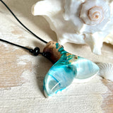 Walflossen-Anhänger „Flossenklang“ – handgefertigtes Unikat aus Maserholz und blau-weißem Harz. Die elegant geschwungene Form erinnert an die Flosse eines Wals und symbolisiert Freiheit, Stärke und Naturverbundenheit. Mit verstellbarem schwarzen Lederband und Onyxperlen gefertigt, ist jedes Stück ein individuelles Schmuckstück für Meeresliebhaber und Natursuchende. Maritimer Halsschmuck, inspiriert vom Ozean, glatt poliert und mit Liebe zum Detail von Hand gearbeitet.
