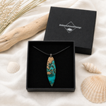 LAGUNENTRAUM Anhänger in schwarzer Schmuckbox von ZeitlosSchmuckDesign, handgefertigter Surfboard-Schmuck aus Maserholz und türkisem Epoxidharz am schwarzen Lederband – maritimer Naturschmuck im Lagunenblau-Look.