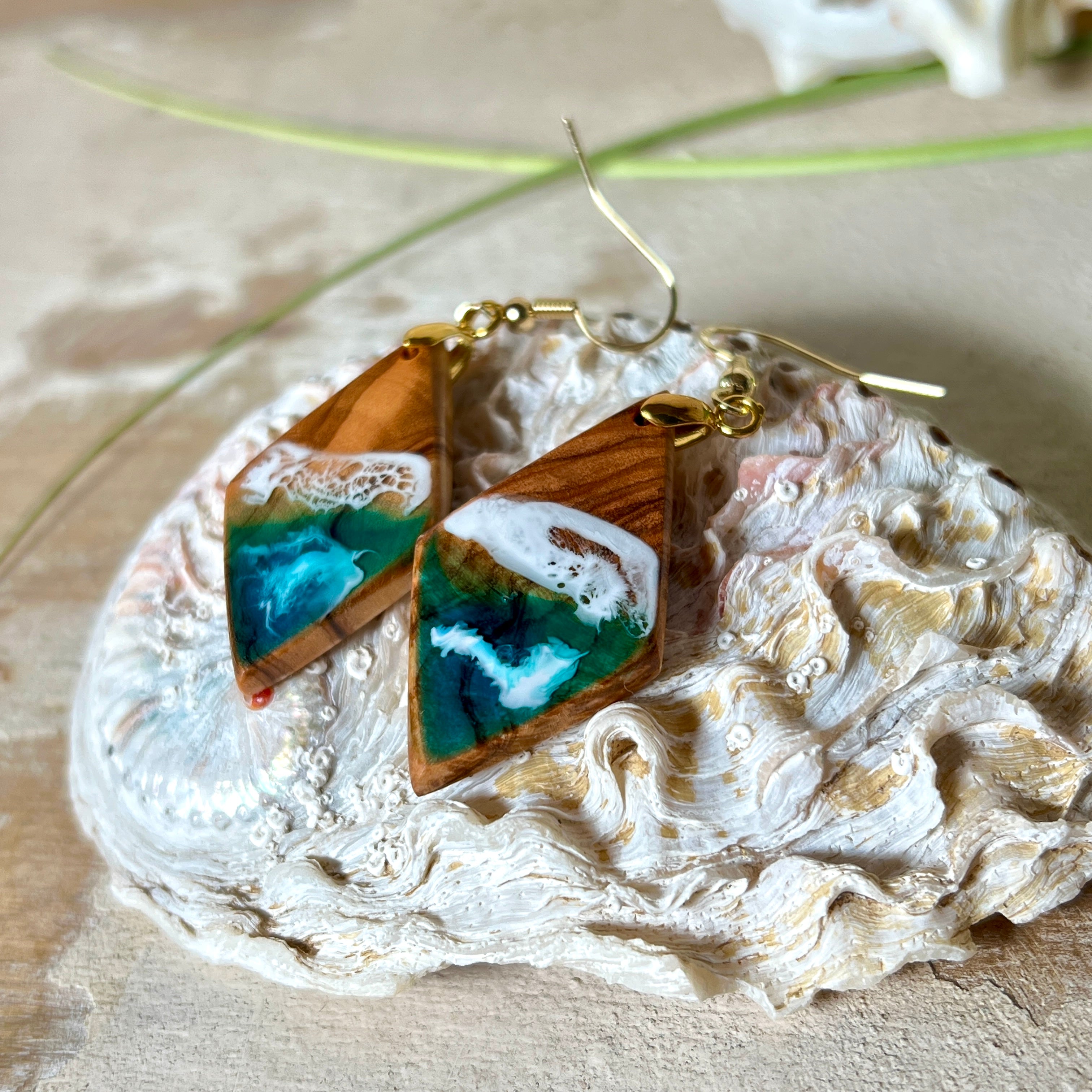Handgefertigte Ohrringe „Ocean Diamond“ aus Olivenholz und Epoxidharz in Diamantform. Türkis-, Blau- und Weißtöne bilden ein wellenartiges Design, inspiriert vom Meer. Jeder Ohrring ist ein Unikat mit individueller Maserung. Vergoldete, nickelfreie und bleifreie Anhängerschlaufe, 925 Sterling Silber Ohrhaken. Maritimer Schmuck für Meerliebhaber und besondere Anlässe.