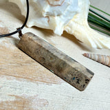 Rechteckiger Stabanhänger aus Maserholz und glasklarem Epoxidharz in tiefen Blau- und Türkistönen mit organischer Lagunen/Riff-Optik. Hochglanzpoliert, ca. 5,3 × 1,2 cm. Der Anhänger hängt an einer schwarzen Lederkette mit Edelstahl-Karabiner und 5-cm-Verlängerung (45 + 5 cm); die Anhängerschlaufe ist ebenfalls aus Edelstahl. Handgefertigtes Unikat, Lieferung in edler Schmuckbox – maritimer Look.