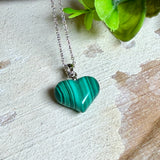 Halskette mit Malachit-Herz: kleiner, gewölbter Herzanhänger aus intensiv grün gebändertem Malachit, ca. 16 x 14 x 10 mm, in hochglanzpolierter, rhodinierter 925 Silberfassung an feiner Ankerkette aus Silber.