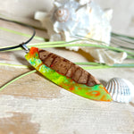 Handgefertigte Halskette „Tropical Glow“ mit Surfbrett-Anhänger aus naturbelassenem Rebholz (Weinrebe) und marmoriertem Epoxidharz in Grün, Orange, Türkis und Weiß. Größe des Anhängers ca. 6,5 × 2 cm. Das Harz fluoresziert eindrucksvoll unter UV-/Schwarzlicht. Edelstahl-Anhängerschlaufe, schwarze Lederkette (45 cm + 5 cm Verlängerung) mit Edelstahl-Karabiner. Unikat in maritim-sommerlichem Stil, ideal als besonderes Geschenk.