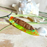 Handgefertigte Halskette „Tropical Glow“ mit Surfbrett-Anhänger aus naturbelassenem Rebholz (Weinrebe) und marmoriertem Epoxidharz in Grün, Orange, Türkis und Weiß. Größe des Anhängers ca. 6,5 × 2 cm. Das Harz fluoresziert eindrucksvoll unter UV-/Schwarzlicht. Edelstahl-Anhängerschlaufe, schwarze Lederkette (45 cm + 5 cm Verlängerung) mit Edelstahl-Karabiner. Unikat in maritim-sommerlichem Stil, ideal als besonderes Geschenk.