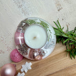 Runder Teelichthalter aus klarem Epoxidharz, Durchmesser ca. 7 cm, Höhe ca. 4 cm. Im Harz sind rosa Weihnachtskugeln, ein Stern, eine Schneeflocke, ein Tannenbaum, künstliche Tannennadeln und feiner Glitzer eingegossen. Vertiefung für ein Teelicht in der Mitte, Unterseite mit vier Korkpads als Möbelschoner. Fotografiert auf Holz mit Tannenzweig und rosa Kugeln als weihnachtliche Dekoration