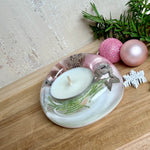 Runder Teelichthalter aus klarem Epoxidharz, Durchmesser ca. 7 cm, Höhe ca. 4 cm. Im Harz sind rosa Weihnachtskugeln, ein Stern, eine Schneeflocke, ein Tannenbaum, künstliche Tannennadeln und feiner Glitzer eingegossen. Vertiefung für ein Teelicht in der Mitte, Unterseite mit vier Korkpads als Möbelschoner. Fotografiert auf Holz mit Tannenzweig und rosa Kugeln als weihnachtliche Dekoration