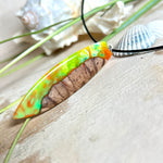 Handgefertigte Halskette „Tropical Glow“ mit Surfbrett-Anhänger aus naturbelassenem Rebholz (Weinrebe) und marmoriertem Epoxidharz in Grün, Orange, Türkis und Weiß. Größe des Anhängers ca. 6,5 × 2 cm. Das Harz fluoresziert eindrucksvoll unter UV-/Schwarzlicht. Edelstahl-Anhängerschlaufe, schwarze Lederkette (45 cm + 5 cm Verlängerung) mit Edelstahl-Karabiner. Unikat in maritim-sommerlichem Stil, ideal als besonderes Geschenk.