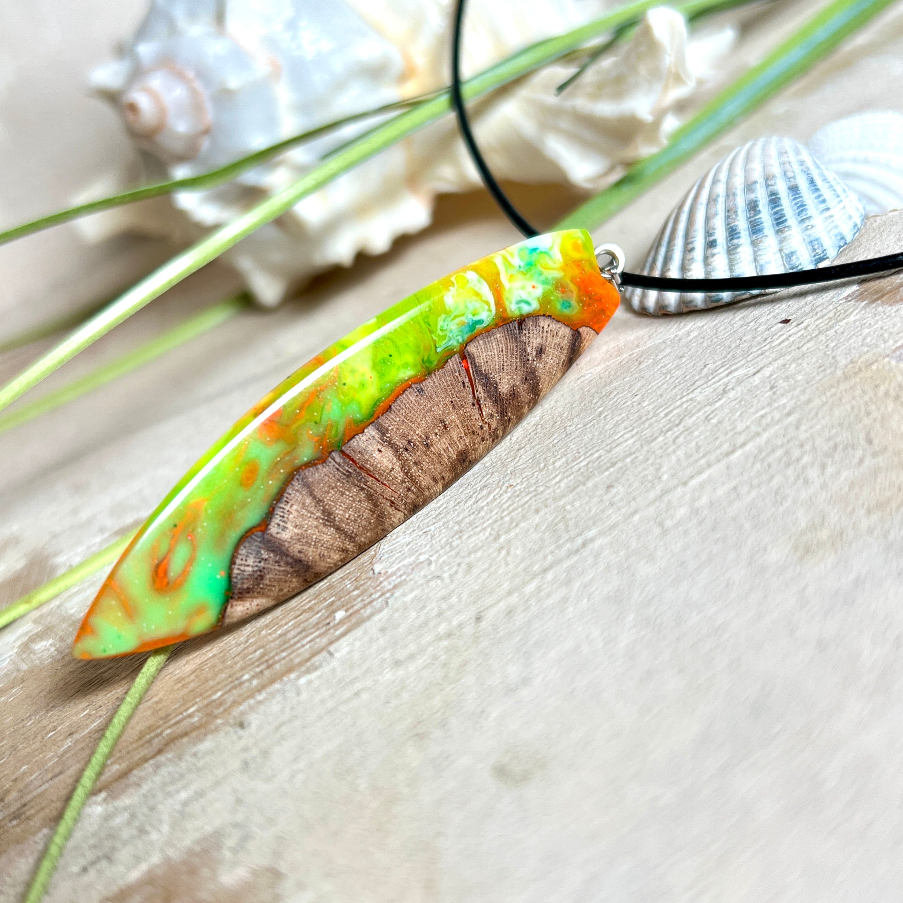 Handgefertigte Halskette „Tropical Glow“ mit Surfbrett-Anhänger aus naturbelassenem Rebholz (Weinrebe) und marmoriertem Epoxidharz in Grün, Orange, Türkis und Weiß. Größe des Anhängers ca. 6,5 × 2 cm. Das Harz fluoresziert eindrucksvoll unter UV-/Schwarzlicht. Edelstahl-Anhängerschlaufe, schwarze Lederkette (45 cm + 5 cm Verlängerung) mit Edelstahl-Karabiner. Unikat in maritim-sommerlichem Stil, ideal als besonderes Geschenk.