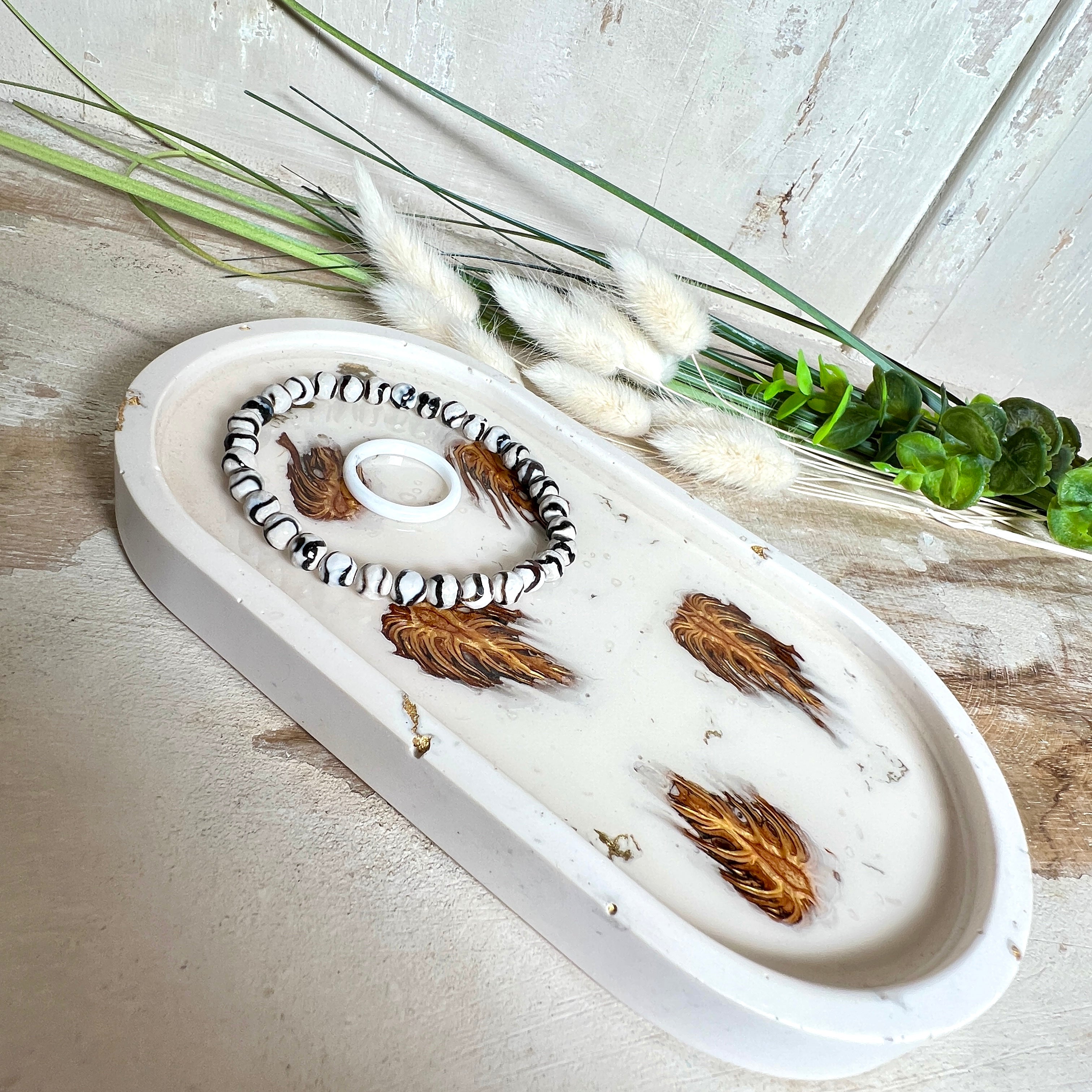 Handgefertigtes Schmucktablett aus Jesmonite mit echten Zapfen, die in einer glänzenden Resin-Schicht eingebettet sind. Die ovale Form und die natürliche Farbgebung machen es zu einem stilvollen Wohnaccessoire. Mit rutschfesten Korkpunkten auf der Unterseite ideal als Ablage für Schmuck, Schlüssel oder Dekoartikel. Jeder Artikel ist ein Unikat aus Handarbeit – Lieferung ohne Dekoration.