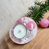 Rosa Teelichthalter aus klarem Epoxidharz, ca. 8 × 6,5 cm, Höhe ca. 4 cm. Im Harz sind kleine rosa Weihnachtskugeln, ein Stern, eine Schneeflocke und rosa Granulat eingegossen. Ovaler Halter für ein Teelicht, Unterseite mit vier runden Korkpads als Möbelschoner. Fotografiert auf Holz mit Tannenzweig und rosa Kugeln als weihnachtlicher Dekohintergrund.