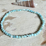 Zartes Larimar-Armband „Lagunenlicht“ mit facettierten 3 mm Perlen aus seltenem Atlantisstein auf Elastikfaden. Die kleinen Larimarsteine zeigen sanfte Blau- und Weißtöne wie Lagunenwasser. Innenumfang ca. 19 cm. Fotografiert auf Muscheln, einem dekorativen Stein und in einer schwarzen Schmuckbox von ZeitlosSchmuckDesign im maritimen Stil.
