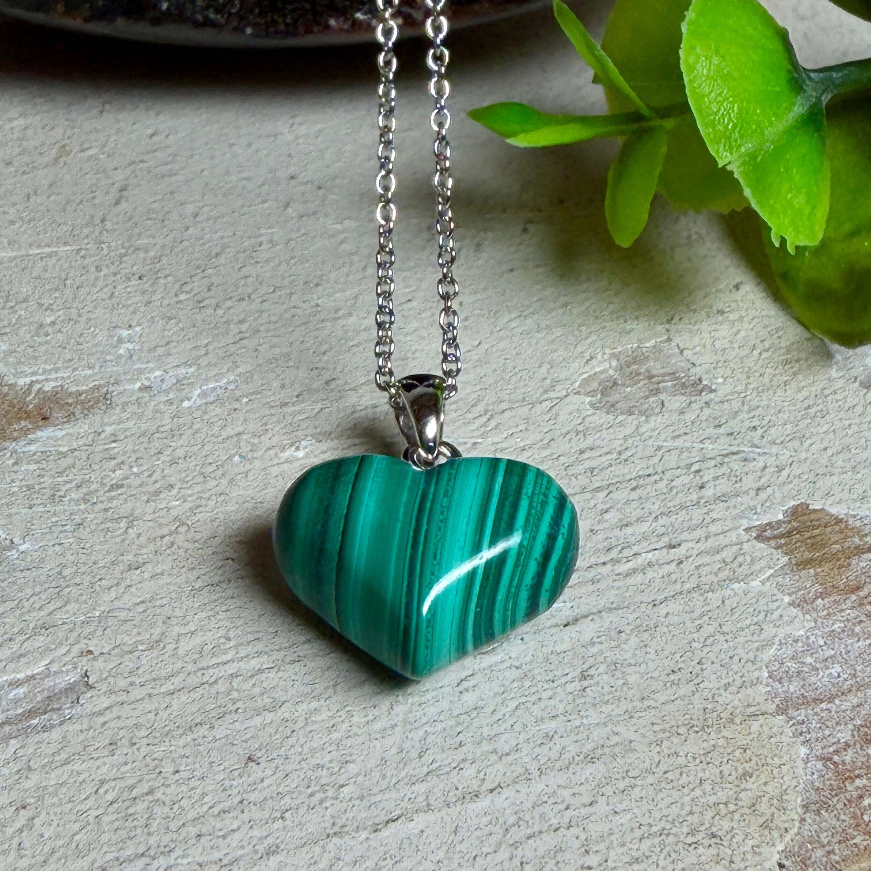 Halskette mit Malachit-Herz: kleiner, gewölbter Herzanhänger aus intensiv grün gebändertem Malachit, ca. 16 x 14 x 10 mm, in hochglanzpolierter, rhodinierter 925 Silberfassung an feiner Ankerkette aus Silber.