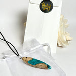 Handgefertigte Surfbrett Kette aus Maserholz und türkisfarbenem Resin mit Edelstahl Anhängerschlaufe an schwarzer Lederkette mit Karabiner und Verlängerung. Filigraner Ocean Anhänger inspiriert von Meer und Wellen, natürlicher Unikat Schmuck für Damen und Herren.