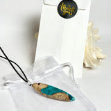 Handgefertigte Surfbrett Kette aus Maserholz und türkisfarbenem Resin mit Edelstahl Anhängerschlaufe an schwarzer Lederkette mit Karabiner und Verlängerung. Filigraner Ocean Anhänger inspiriert von Meer und Wellen, natürlicher Unikat Schmuck für Damen und Herren.