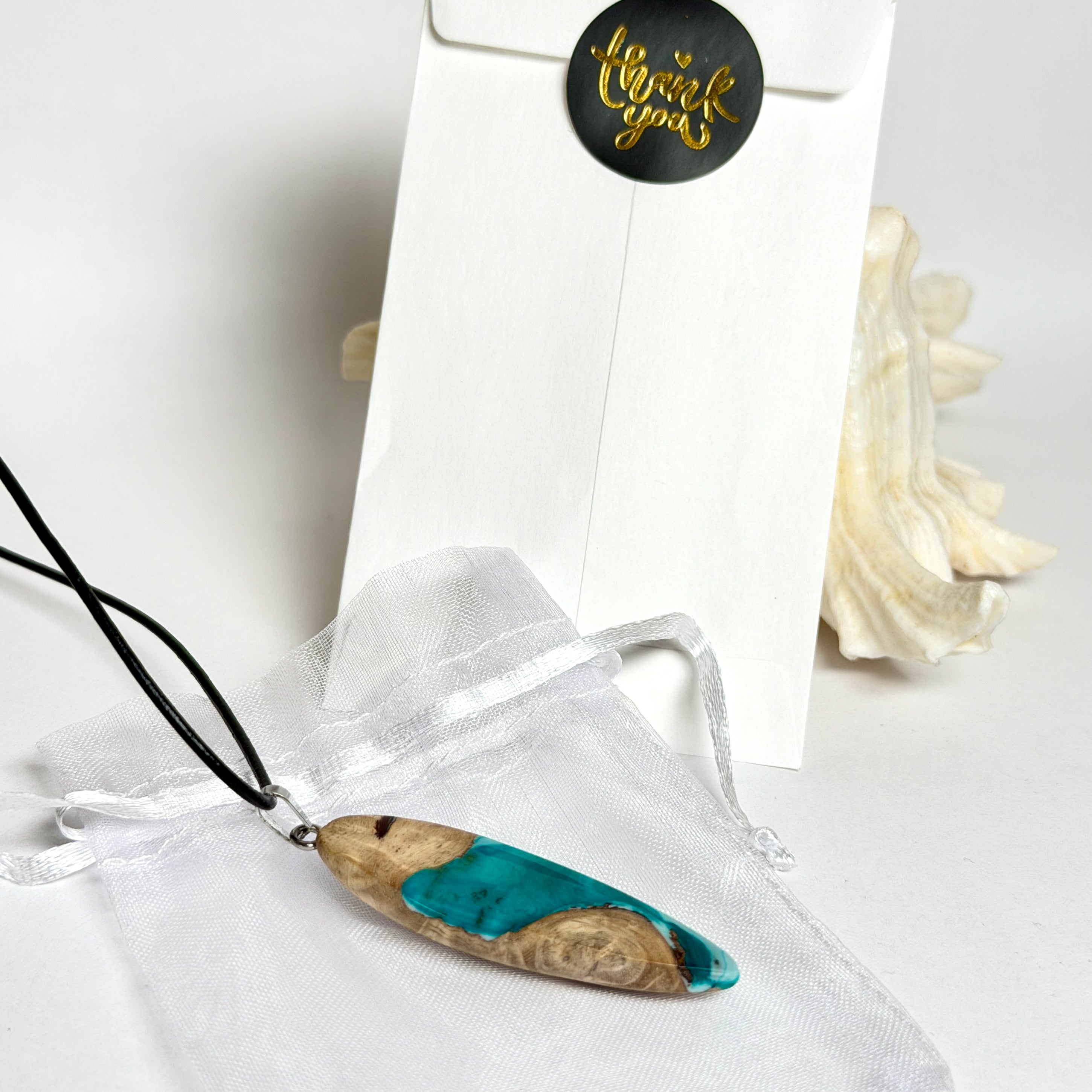 Handgefertigte Surfbrett Kette aus Maserholz und türkisfarbenem Resin mit Edelstahl Anhängerschlaufe an schwarzer Lederkette mit Karabiner und Verlängerung. Filigraner Ocean Anhänger inspiriert von Meer und Wellen, natürlicher Unikat Schmuck für Damen und Herren.