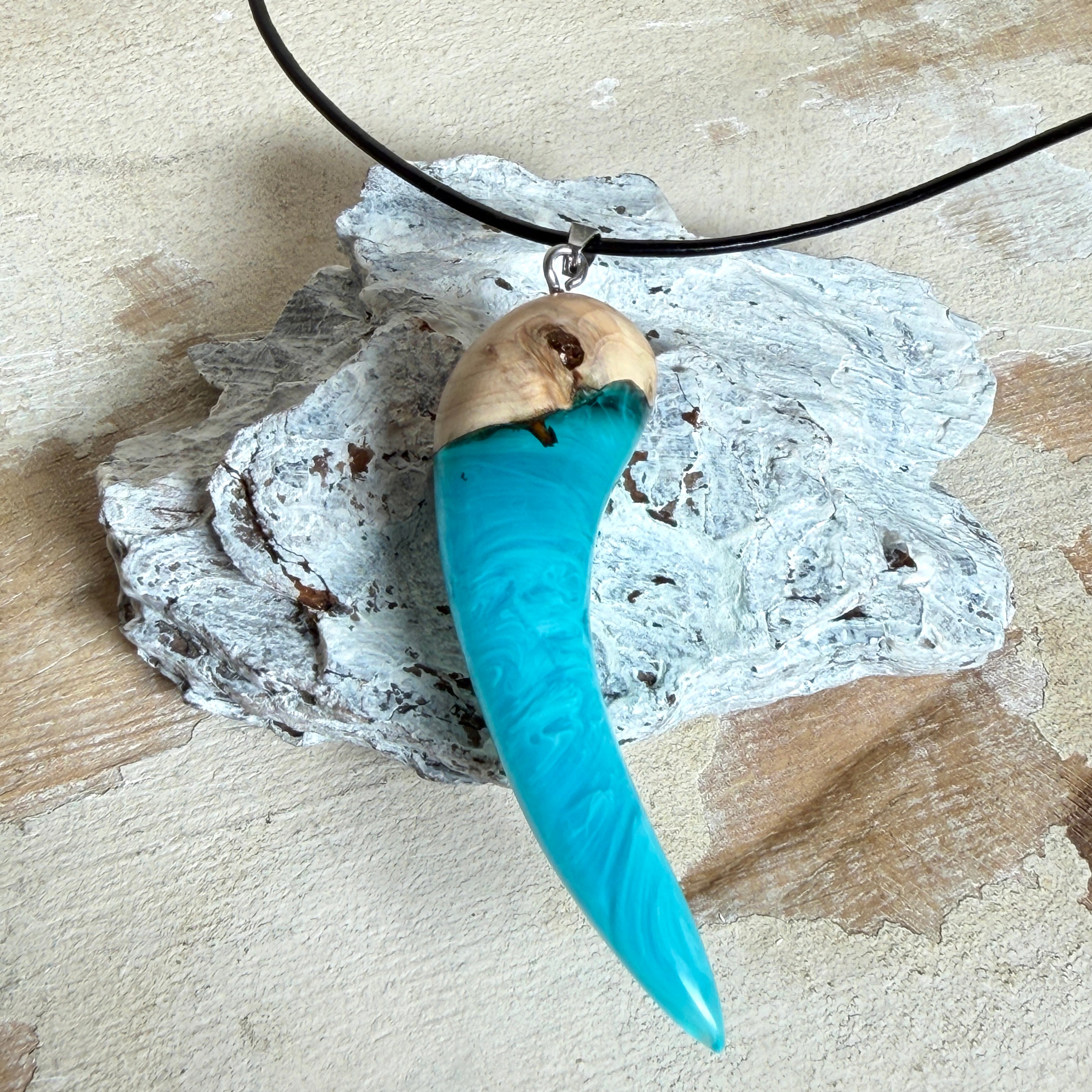 Handgefertigter Anhänger aus Edelholz und transparent-türkisblauem und weißen Epoxidharz, glatt poliert. Größe ca. 6,5 × 2,0 cm. Mit Edelstahlöse an schwarzer Lederkette (45 cm + 5 cm Edelstahl-Verlängerung, Karabiner). Moderner, unisex tragbarer Schmuck mit natürlicher Holzmaserung; kleine Lufteinschlüsse sind charakteristisch.