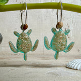 Türkisfarbene Schildkröten-Creolen an feinen 16-mm-Ringen aus 925 Silber, jeweils mit echtem Strandsand im Harz eingebettet und mit kleinen Jaspis-Edelsteinperlen verziert; handgefertigtes Unikat mit sommerlich-maritimem Look, fotografiert als Freisteller, Nahaufnahme oder auf dekorativem Untergrund.
