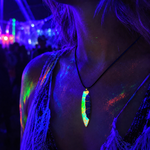 KI-generiertes Tragebild auf einem Festival unter Schwarzlicht: handgefertigter Surfbrett-Anhänger „Tropical Glow“ aus Rebholz und fluoreszierendem Epoxidharz in Grün, Orange, Türkis und Weiß, gerade hängend an schwarzer Lederkette, leuchtender Unikat-Schmuck im Neon-UV-Licht.