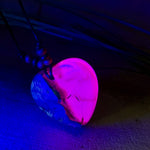 Handgefertigter Herzanhänger aus Olivenholz und leuchtend pinkem Epoxidharz mit eingeschlossenen Pusteblumensamen. Verstellbares braunes Lederband mit Holzperlen, Anhänger ca. 3,5 × 3,3 cm groß. Das Harz leuchtet dezent unter Schwarzlicht. Ein einzigartiges Unikat von ZeitlosSchmuckDesign, inspiriert von Kindheitsglück und Pusteblumen.