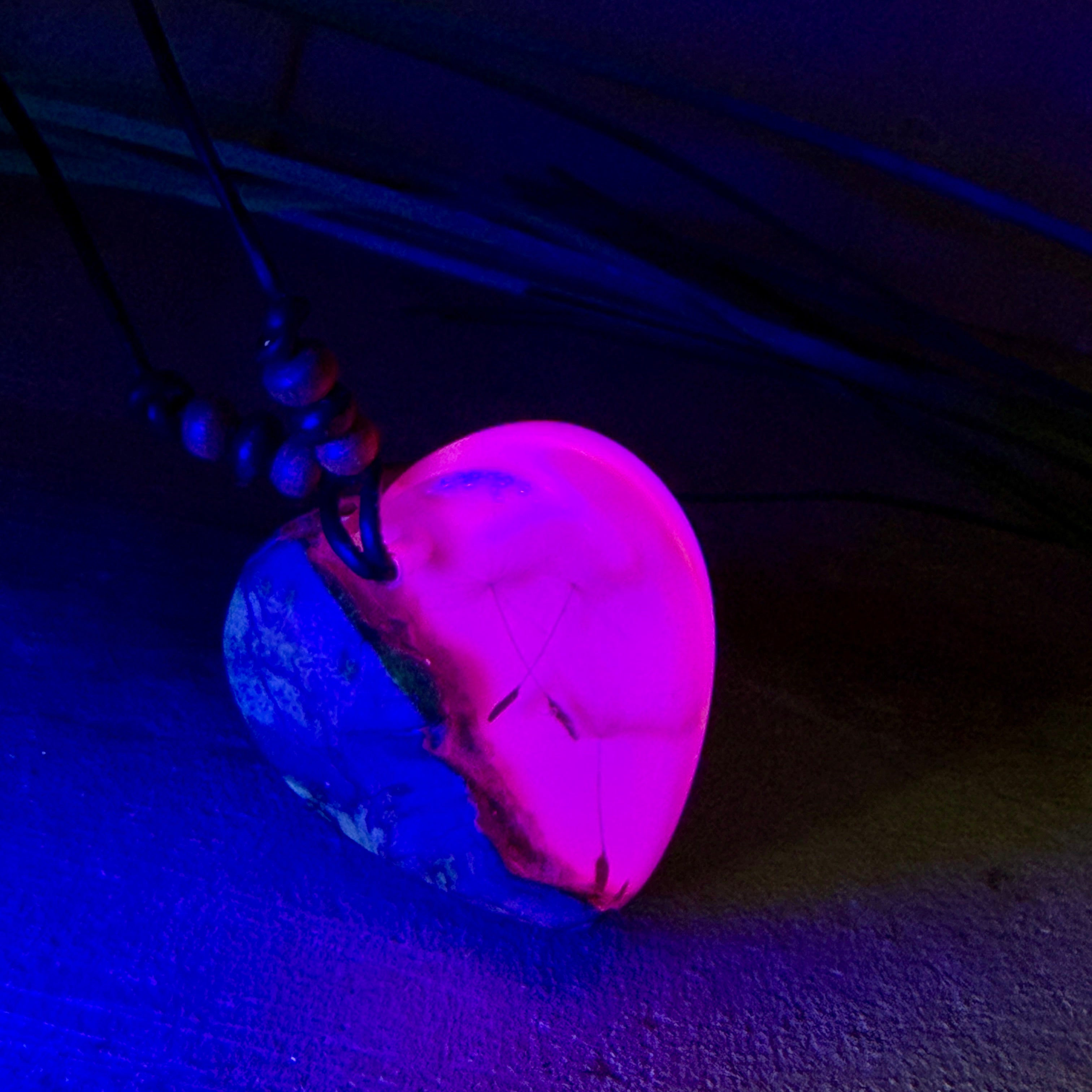 Handgefertigter Herzanhänger aus Olivenholz und leuchtend pinkem Epoxidharz mit eingeschlossenen Pusteblumensamen. Verstellbares braunes Lederband mit Holzperlen, Anhänger ca. 3,5 × 3,3 cm groß. Das Harz leuchtet dezent unter Schwarzlicht. Ein einzigartiges Unikat von ZeitlosSchmuckDesign, inspiriert von Kindheitsglück und Pusteblumen.