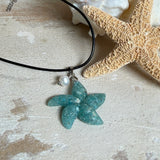 Seestern-Anhänger aus transparentem Harz mit echtem Meersand ( leicht eingefärbt), in blautürkis Strand-Look, mit kleiner Süßwasserperle als Anhänger-Detail. Edelstahlöse, schwarze Lederkette mit Edelstahl-Karabiner und Verlängerung (45 cm + 5 cm). Anhänger ca. 3,5 × 3,5 cm. Handgefertigtes Unikat; vereinzelt kleine Luftbläschen möglich, typisch für Handarbeit.