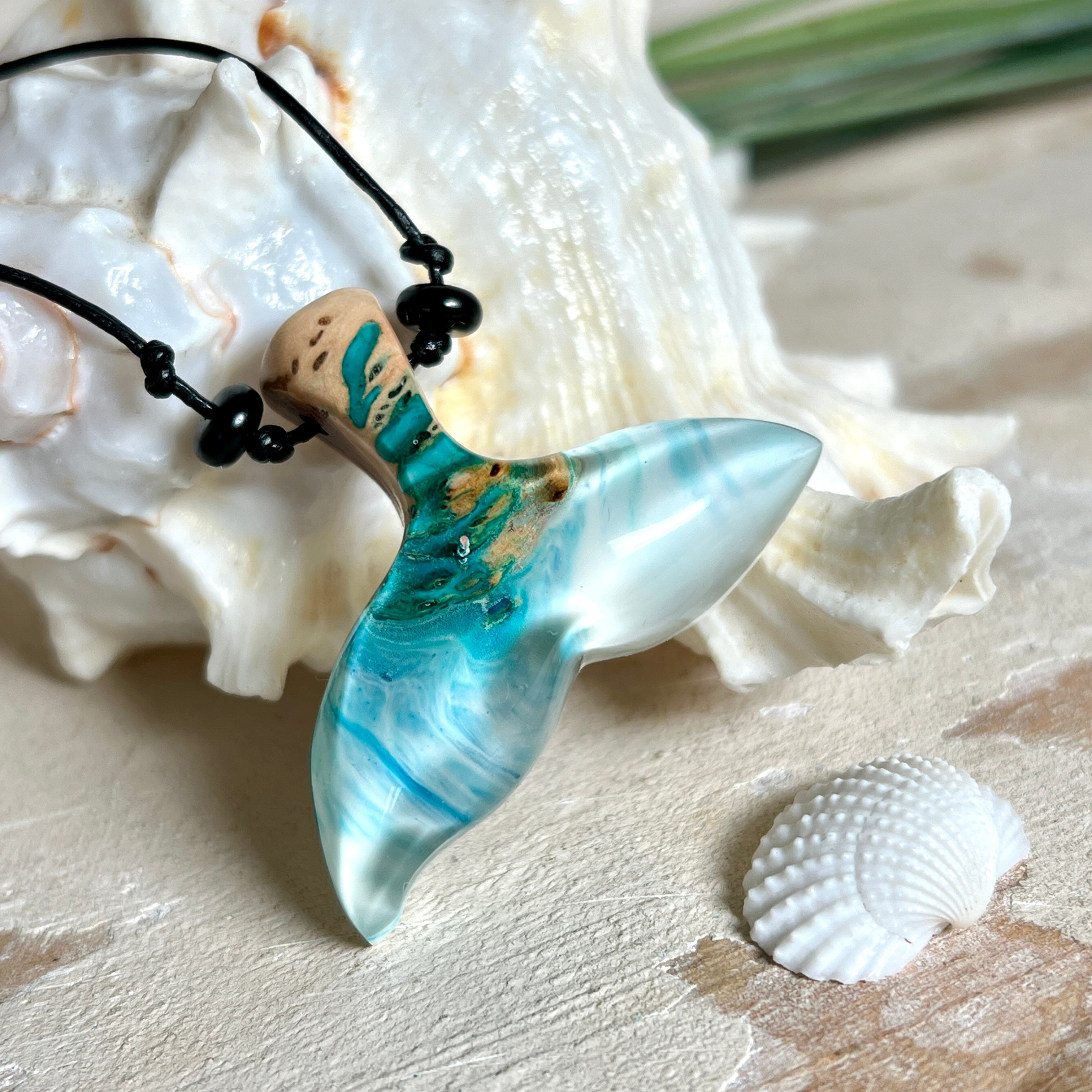 Walflossen-Anhänger „Flossenklang“ – handgefertigtes Unikat aus Maserholz und blau-weißem Harz. Die elegant geschwungene Form erinnert an die Flosse eines Wals und symbolisiert Freiheit, Stärke und Naturverbundenheit. Mit verstellbarem schwarzen Lederband und Onyxperlen gefertigt, ist jedes Stück ein individuelles Schmuckstück für Meeresliebhaber und Natursuchende. Maritimer Halsschmuck, inspiriert vom Ozean, glatt poliert und mit Liebe zum Detail von Hand gearbeitet.