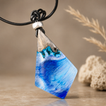 WAVE WHISPER – handgefertigter Holz-Harz-Anhänger aus Maserholz und blau-weißem Epoxidharz, maritimer Naturschmuck am schwarzen Lederband, clean inszeniert mit dezenter Stranddeko